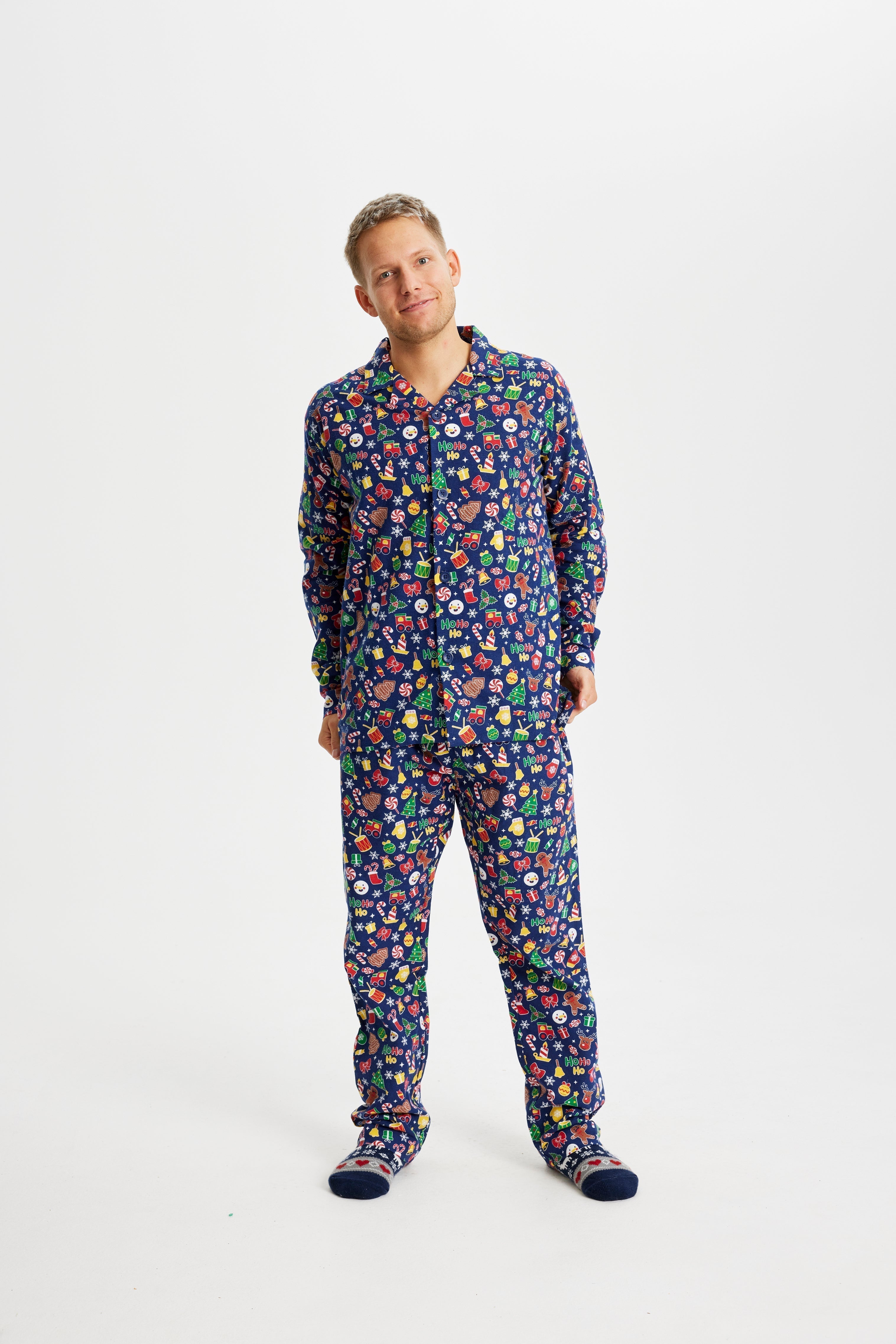 Un homme, les mains dans les poches, portant un pyjama de Noël bleu avec un imprimé de Noël.